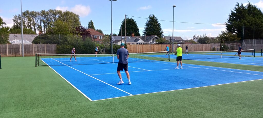 Doubles games on the blue hard tennis courts, with floodlights around the courts