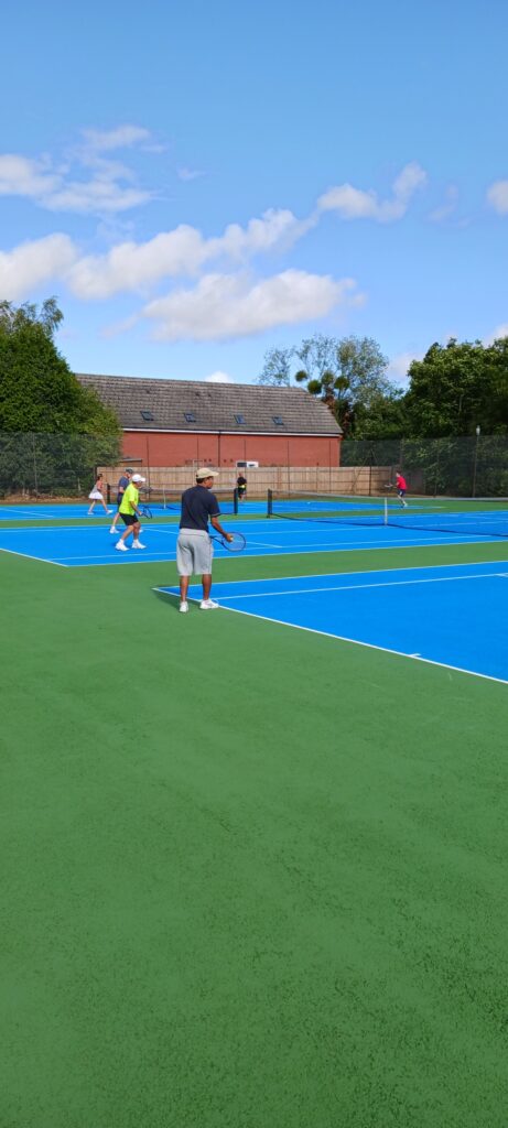 A player about to serve on the tennis courts on a sunny day, with other games in the background